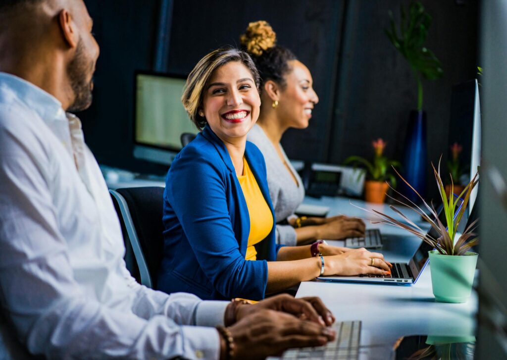 Employees chat and smile with a new temporary employee at their desks