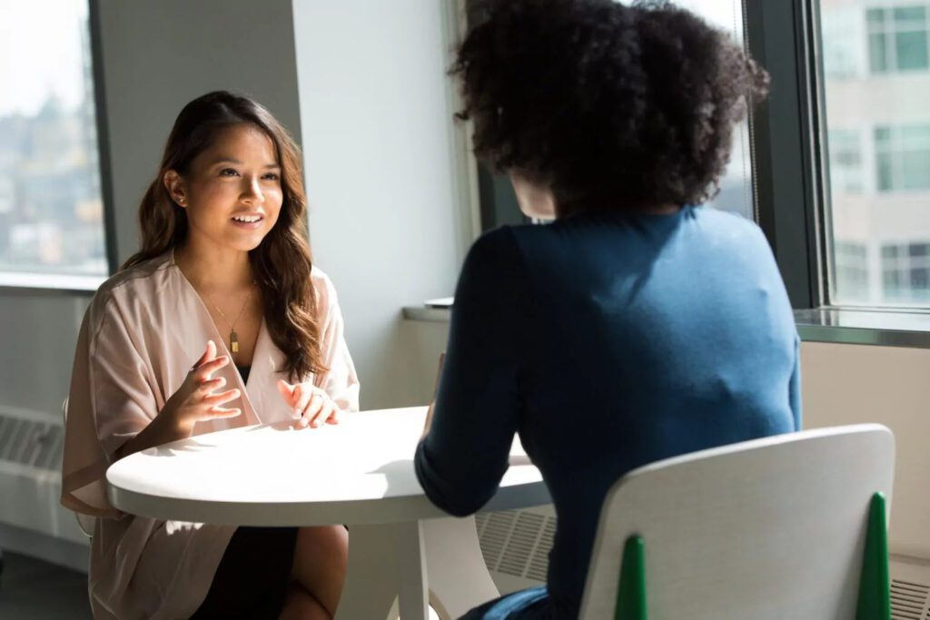 Two women coworkers meeting at a small conference table by an office window